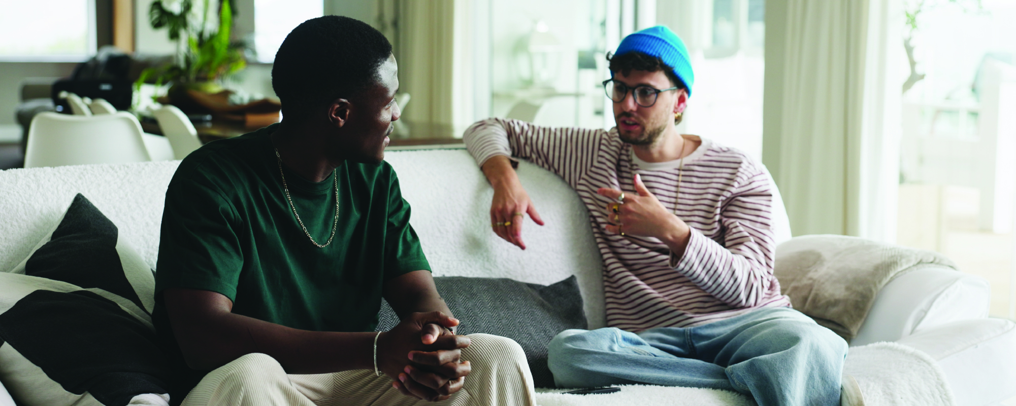 Two men sitting on a couch, engaged in conversation in a bright living room.